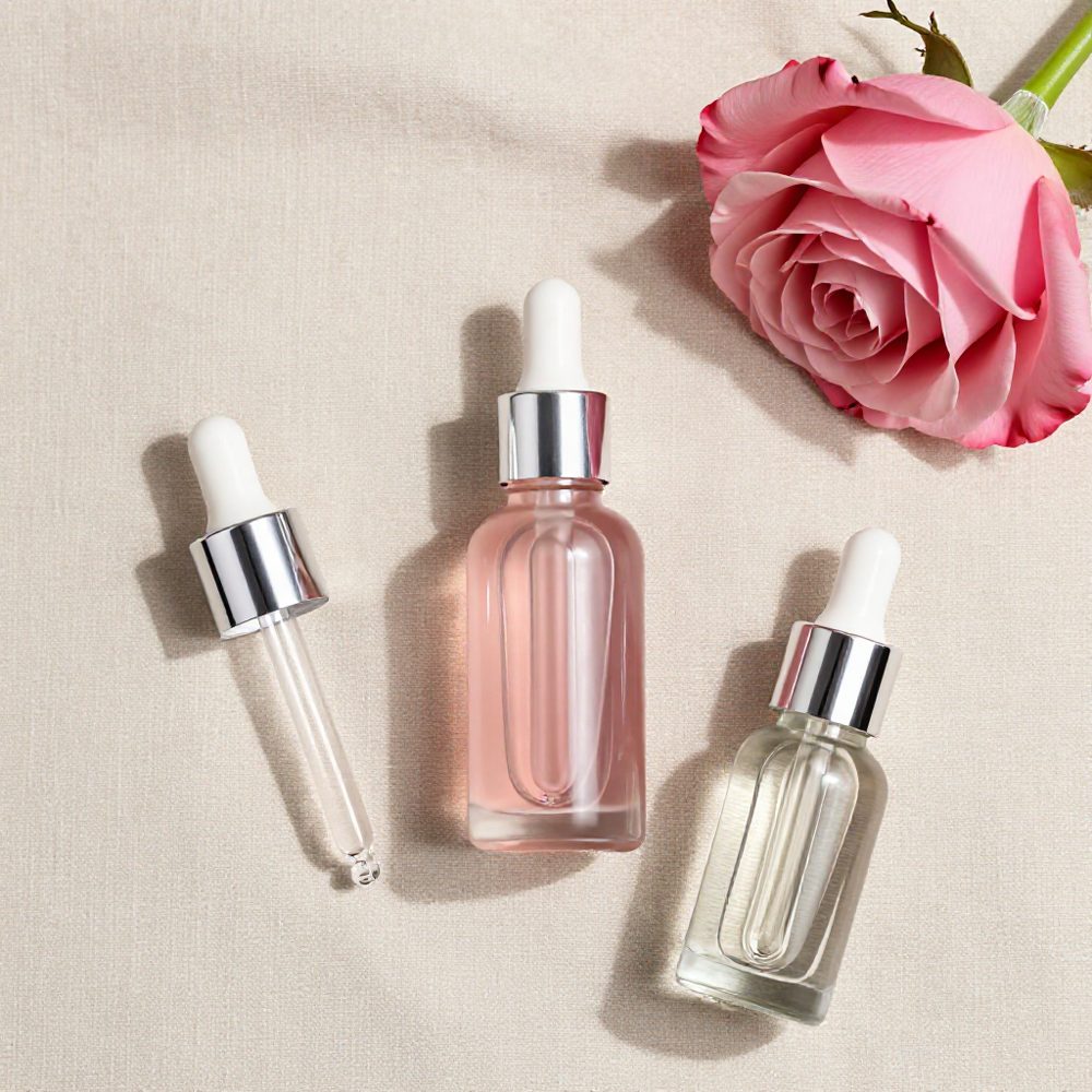 Pink and clear dropper bottles beside a rose on linen